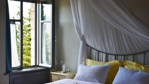 A bedroom with a bed, a nightstand, a window with curtains, and a canopy over the bed. - KIRIAKI GUESTHOUSE & SUITES (Amfikleia-Elateia)