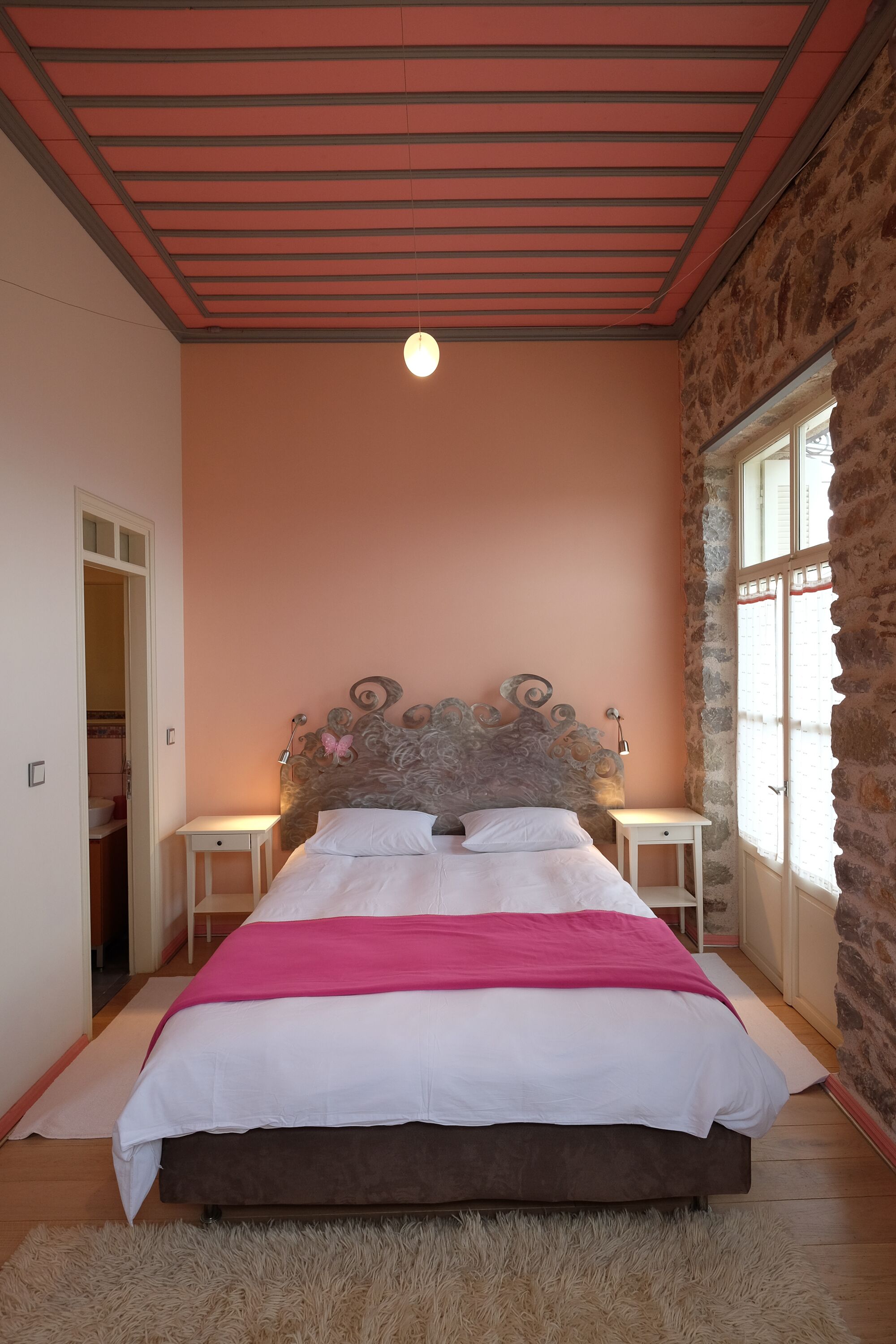 Un dormitorio con cama, cabecera, mesitas de noche, una ventana y una puerta.
