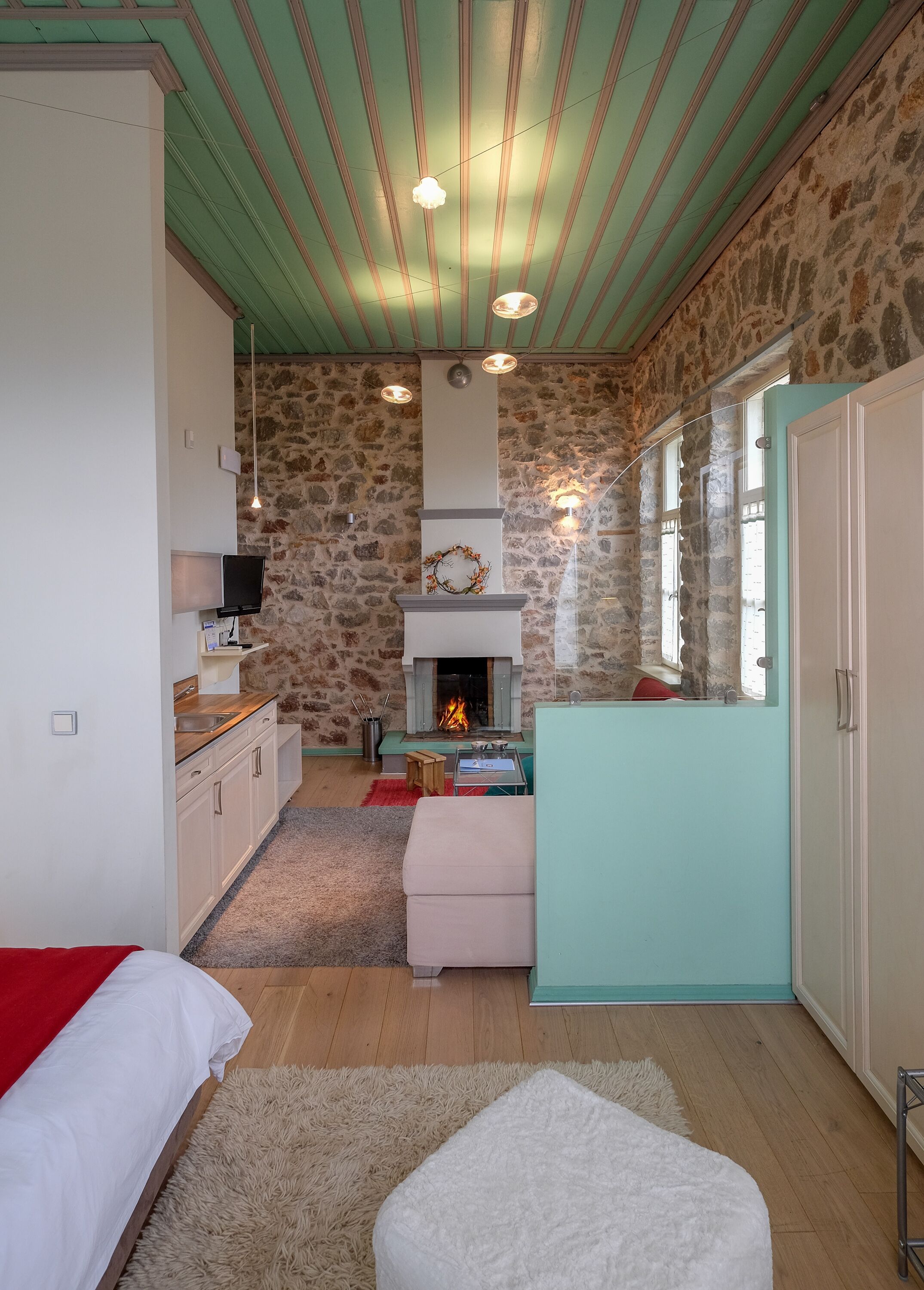 A room with a stone wall, a fireplace, a bed, a table, and a window.
