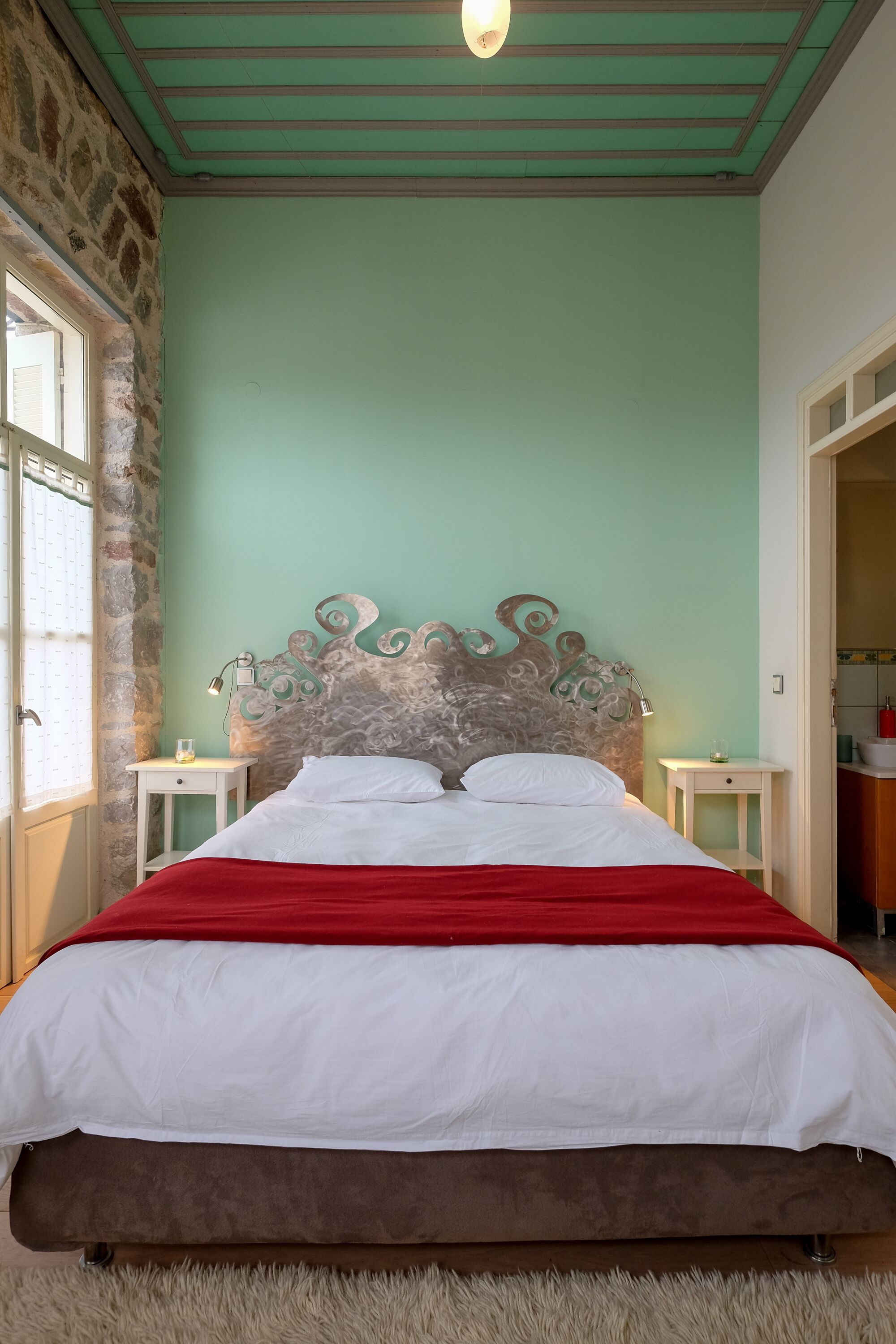 A bed with a red blanket, a stone wall, and a green ceiling.