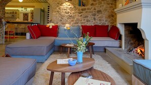 A cozy living room with a stone wall, a fireplace, and a modern sofa set. - KIRIAKI GUESTHOUSE & SUITES (Amfikleia-Elateia)
