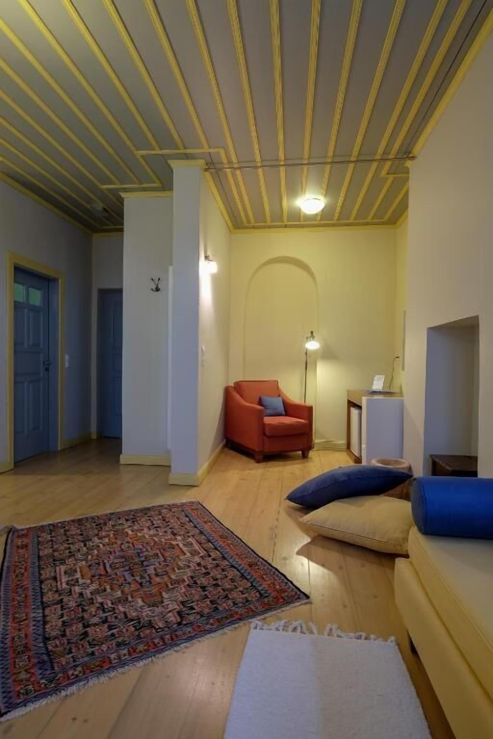 A hallway with a red armchair, a white rug, and a sofa with blue cushions.