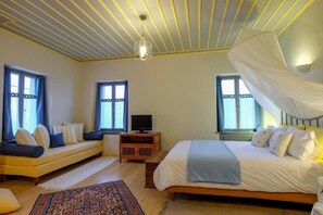 Une chambre à coucher avec un lit, une télévision, un canapé et une fenêtre avec des rideaux.