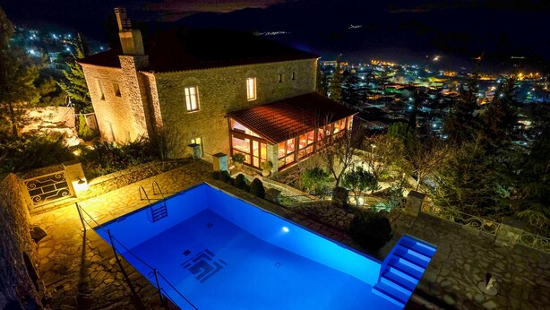 A stone building with a swimming pool, a wooden deck, and a view of a town at night. - KIRIAKI GUESTHOUSE & SUITES (Amfikleia-Elateia)