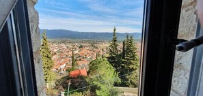 Une vue depuis une fenêtre donnant sur une ville avec des bâtiments aux toits rouges, des arbres et des montagnes à l’horizon.