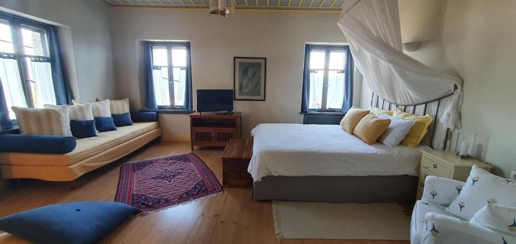 A bedroom with a bed, a sofa, a TV, and a window.