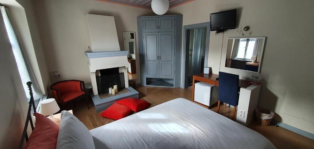 Ein Schlafzimmer mit Bett, einem roten Sessel, Kamin, Kleiderschrank, Schreibtisch und Fernseher.