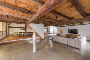 Um loft espaçoso com vigas de madeira aparentes, área de jantar, sala de estar com sofá e televisão.