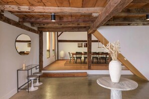 Ein Zimmer mit Holzbalkendecke, einem runden Tisch mit einer Vase und einer Treppe, die in einen anderen Bereich führt.