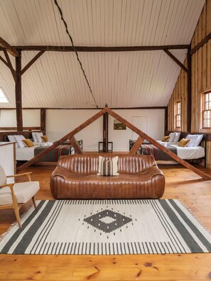 Ein Loft-Zimmer mit schrägverdeckter Decke, Holzbalken, einem zentral platzierten braunen Ledersofa und einem gemusterten Teppich.