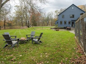 Ein blaues Haus mit umzäuntem Garten, zwei Adirondack-Stühlen und einer Feuerstelle.