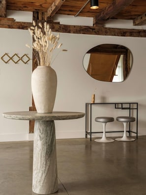 Ein modernes Interieur mit einem Marmortisch, einer Vase mit Trockenpflanzen, einem Spiegel und zwei Hocker.