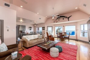 A spacious living area with a high ceiling, a dining table with chairs, a sofa, and a coffee table. - Casa Copano by Miss Kitty’s (Rockport)