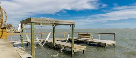 A wooden pier extending into calm water with a bench and hammock.