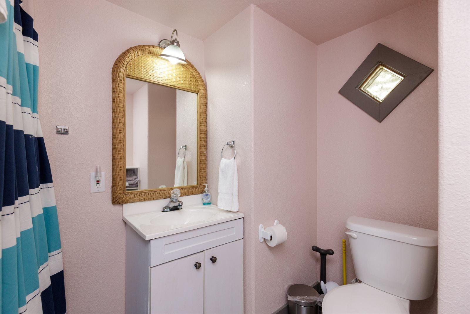 A bathroom with a white sink, a gold-framed mirror, a toilet, and a small window.