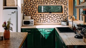 Uma cozinha moderna com vigas de madeira, uma parede de troncos, armários verdes e micro-ondas embutido.
