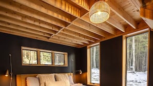 Quarto aconchegante com cama de madeira, janelas amplas e luminária no teto.
