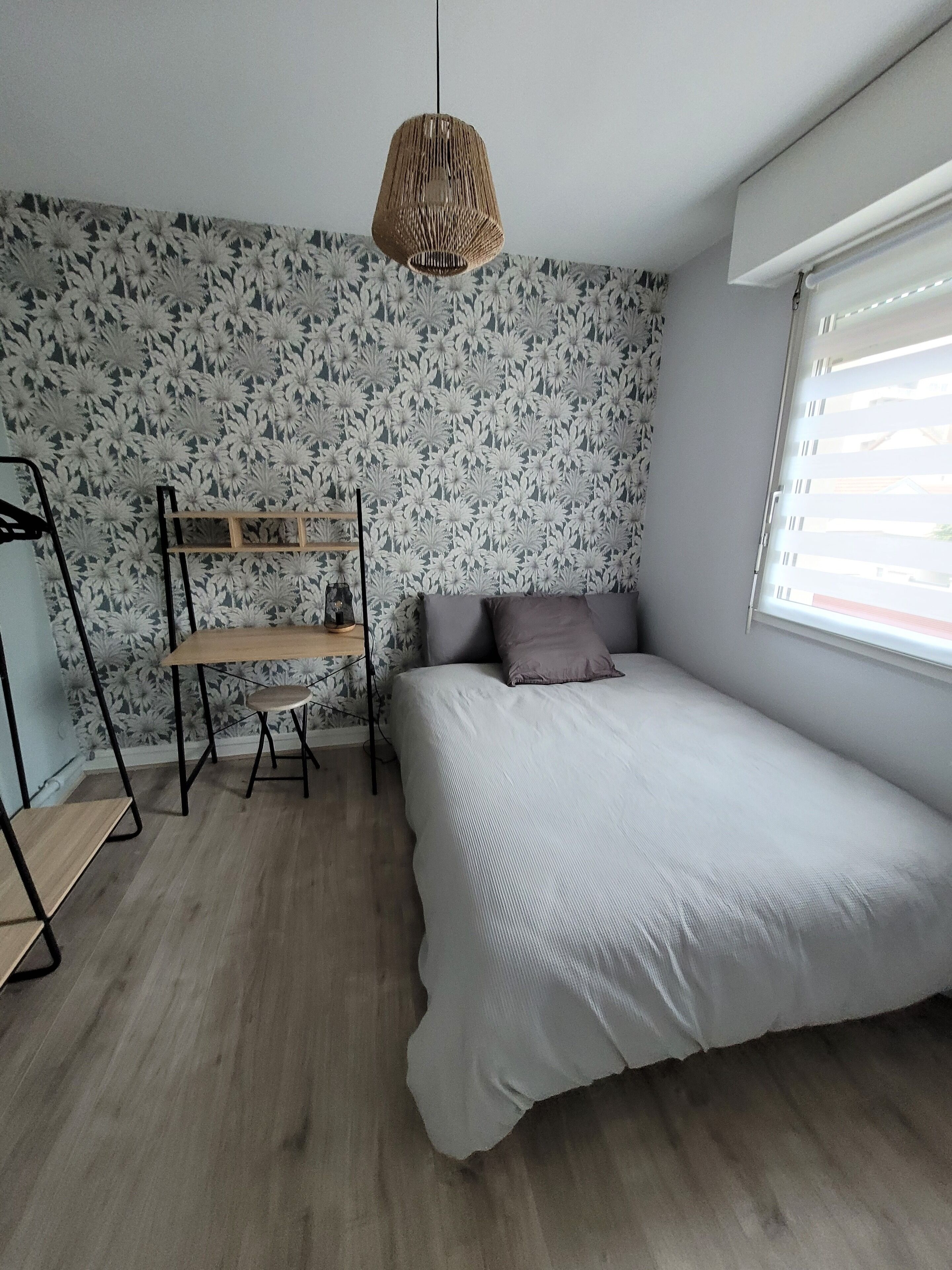 Et soveværelse med en seng, en hængende lampe, en træhylde og et vindue med persienner.