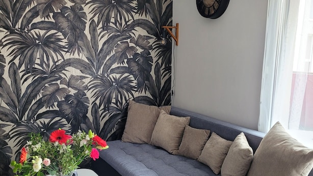 En moderne stue med en grå sofa, et hvidt bord og blomstret tapet.