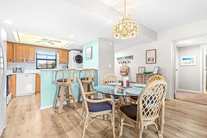 A modern kitchen with wooden cabinets, a built-in oven, and a dining area with wicker chairs and a glass table.