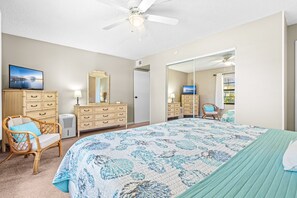 A bedroom with a large bed, two bedside tables, a dresser, a chair, a television, and a ceiling fan.