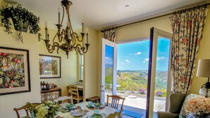 A dining area with a table set for four, a chandelier, and a view of the outdoors. - Beverly's Retreat (Fallbrook)