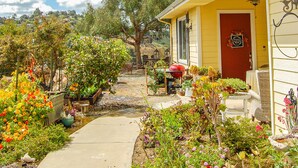 A yellow house with a red door, surrounded by a garden with various plants and flowers. - Beverly's Retreat (Fallbrook)