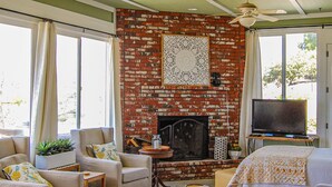 A cozy living room with a brick fireplace, comfortable seating, and a television. - Beverly's Retreat (Fallbrook)