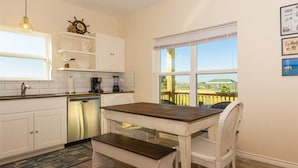 Una cocina con armarios blancos, una mesa de madera y una silla de mimbre.