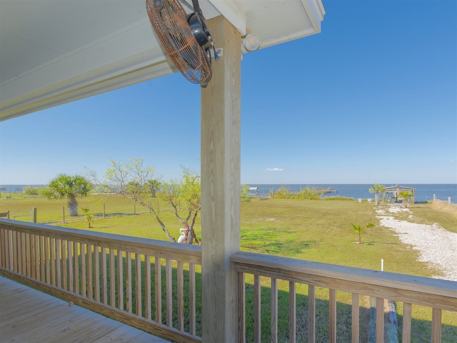 A wooden deck with a view of a grassy area and the ocean.