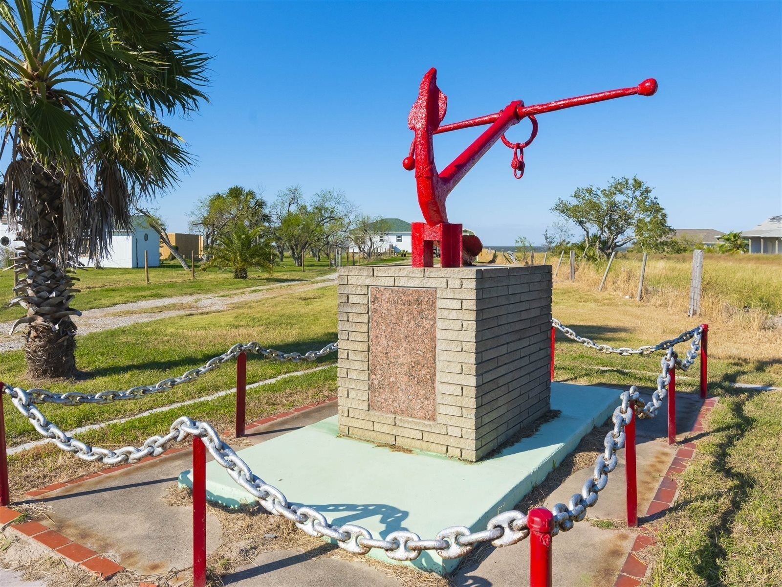 Une sculpture rouge, posée sur un piédestal en briques et entourée d’une clôture en treillis métallique.