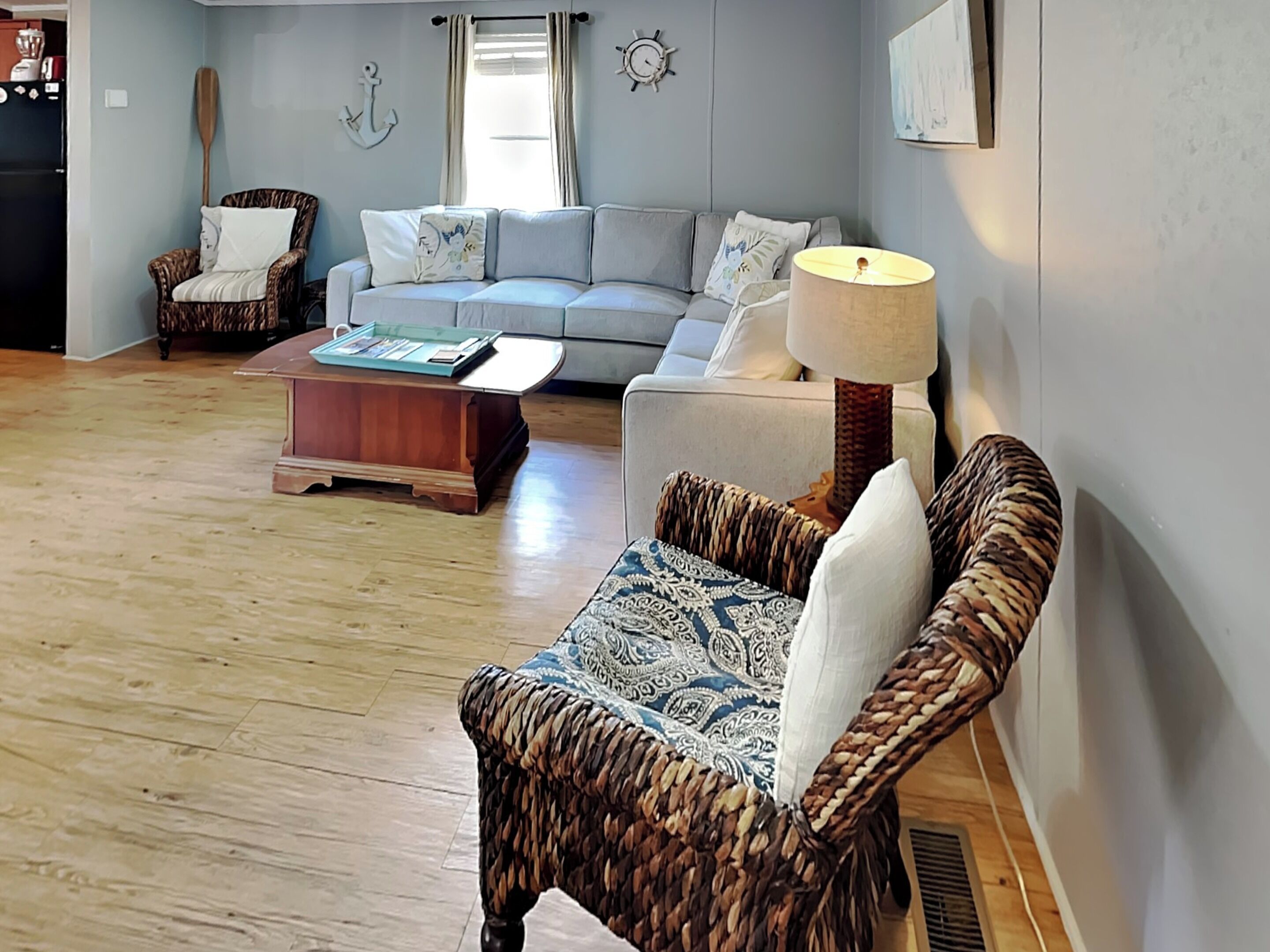 A living room with a grey sofa, a wicker armchair, a wooden coffee table, and a floor lamp.