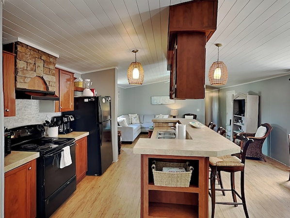 A modern kitchen with wooden cabinets, a black refrigerator, a stove, and hanging pendant lights.