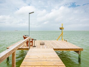 A wooden pier extending into calm waters with a bench and a street lamp.