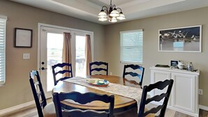 A dining room with a round table, six chairs, and a chandelier. - A Fin N Feather by Miss Kitty’s (Rockport)
