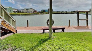 A covered outdoor area with a view of a lake, a wooden deck, and a grassy area. - A Fin N Feather by Miss Kitty’s (Rockport)