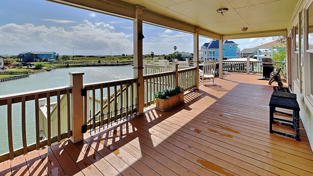 A wooden deck with a railing overlooking a body of water, surrounded by greenery and residential buildings. - A Fin N Feather by Miss Kitty’s (Rockport)