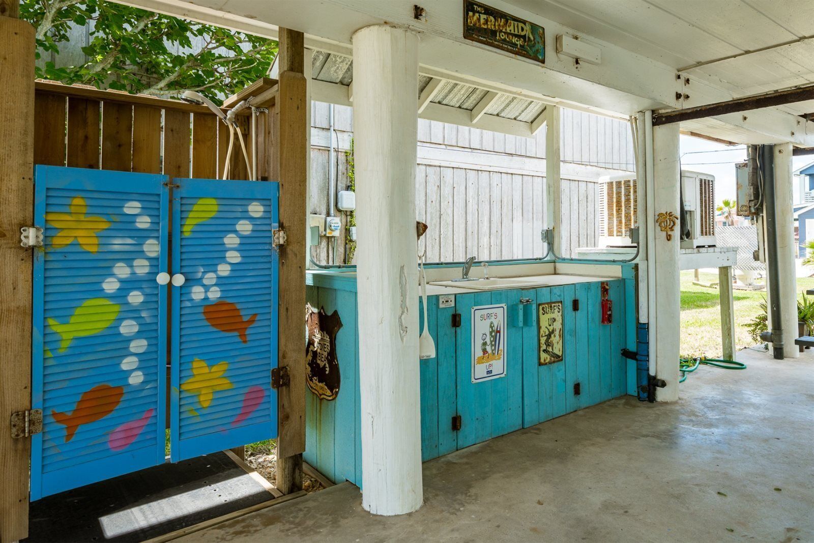 A covered outdoor area with a blue and turquoise color scheme, featuring a sign for 'The Mermaid Lounge'.