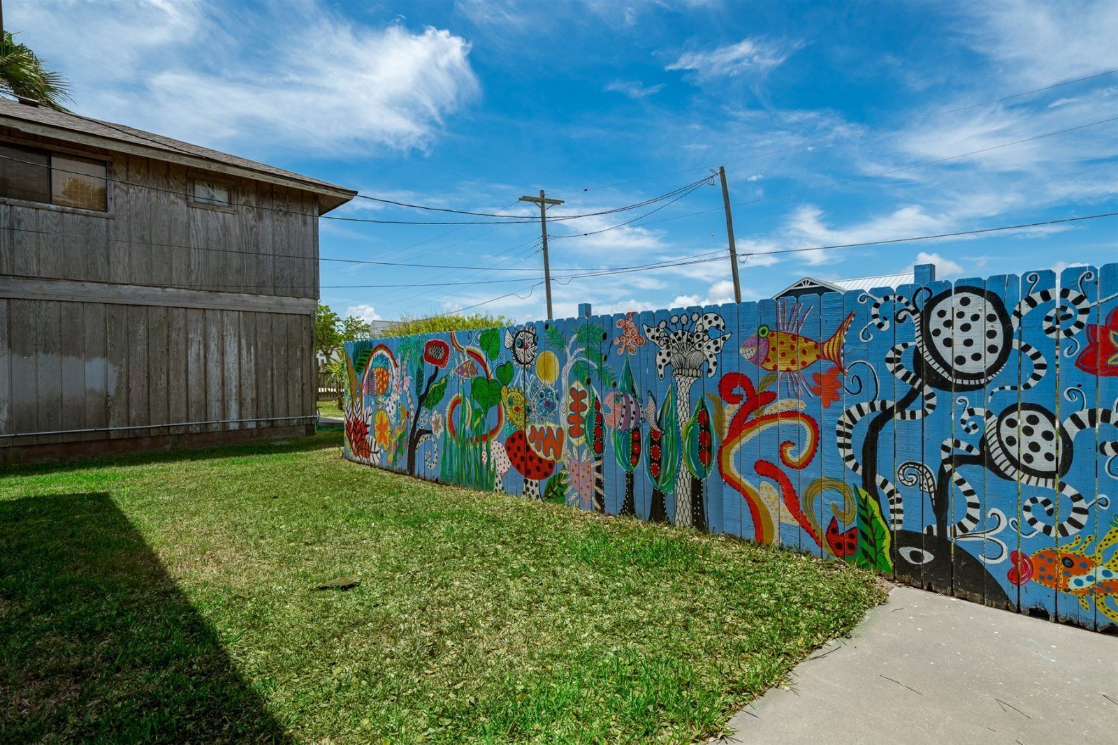 Un mural colorido en una valla con un área verde al frente.