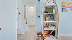 A hallway with a bookshelf filled with books and games, a framed painting, and a rope-wrapped shelf.