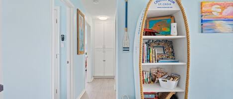 A hallway with a bookshelf filled with books and games, a framed painting, and a rope-wrapped shelf.