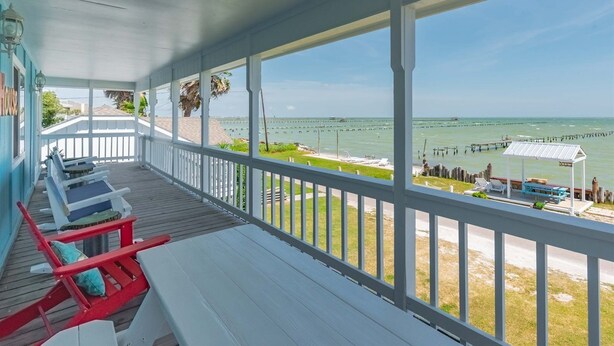 A covered porch with white railings, a view of the ocean, and a few lounge chairs.