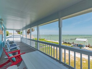 A covered porch with white railings, a view of the ocean, and a few lounge chairs. - Moon Mirror Bay by Miss Kitty’s (Rockport)
