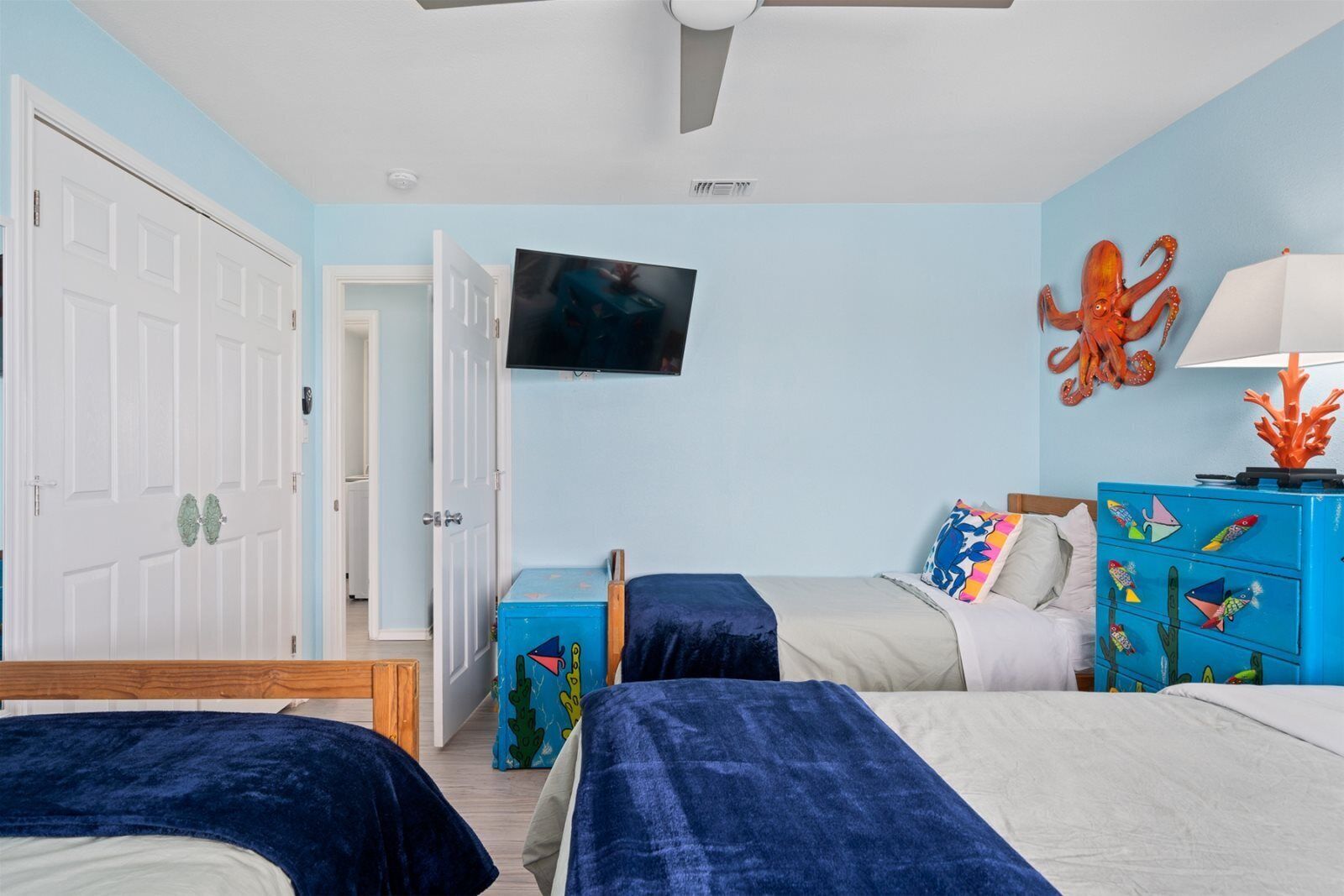 Een slaapkamer met twee bedden, een televisie en een blauwe wand met een octopus decoratie.