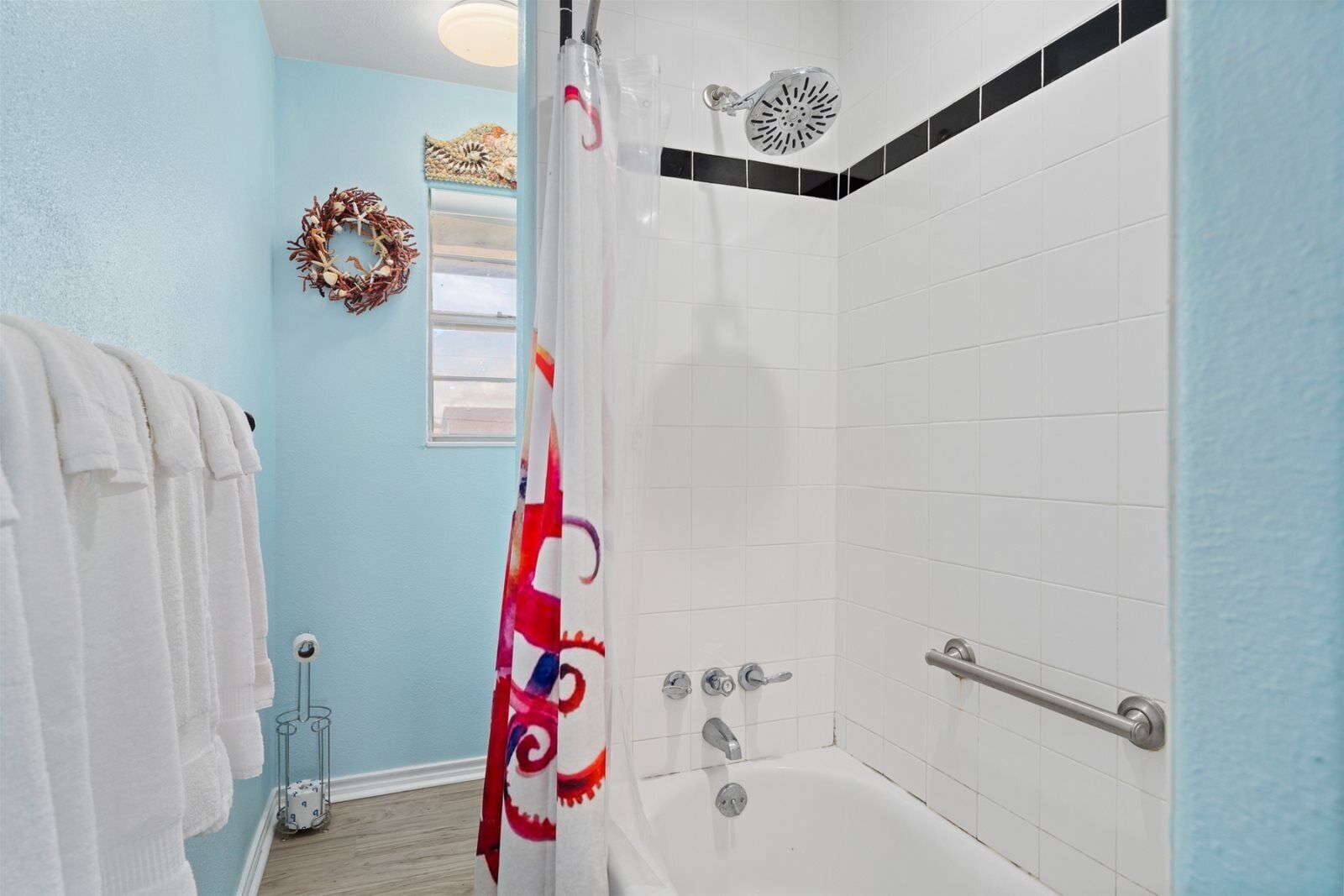 A bathroom with a white bathtub, a shower with a handheld showerhead, and a towel rack with white towels.