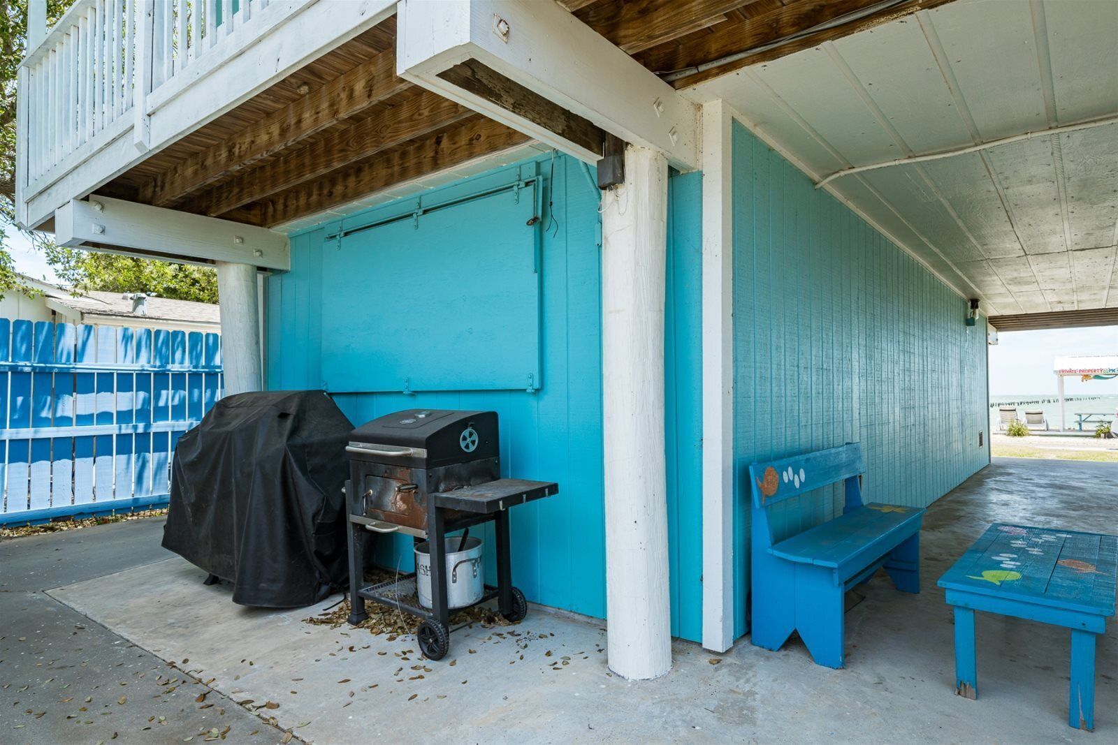 A covered outdoor area with a blue bench, a grill, and a table.