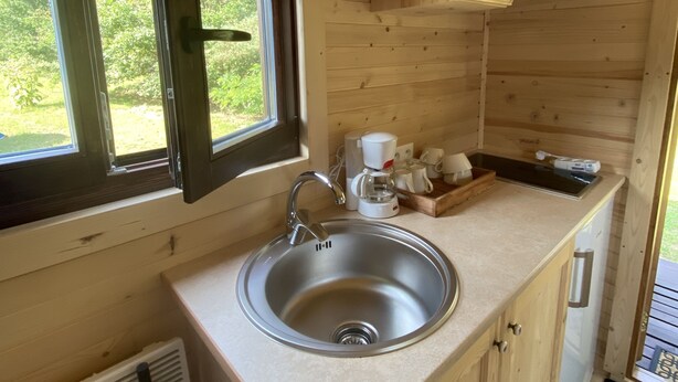 A compact kitchen with a stainless steel sink, wooden cabinets, a window, and a coffee maker. - Roulotte "cecile" Pour un Séjour Atypique en Roulotte (Digoin)