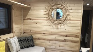 A wooden cabin interior with a bed, a mirror with a sunburst design, and a small bathroom. - Roulotte "cecile" Pour un Séjour Atypique en Roulotte (Digoin)