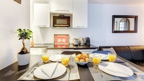 A breakfast setup with croissants, orange juice, and a coffee maker in a modern kitchen with white cabinets and a wooden ceiling. - Chic Marais Retreat | Steps to Cafes & Notre Dame (Paris)