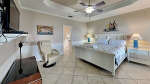 A bedroom with a bed, a chair, a desk, a ceiling fan, and a painting on the wall. - Pelican Point by Miss Kitty’s (Rockport)